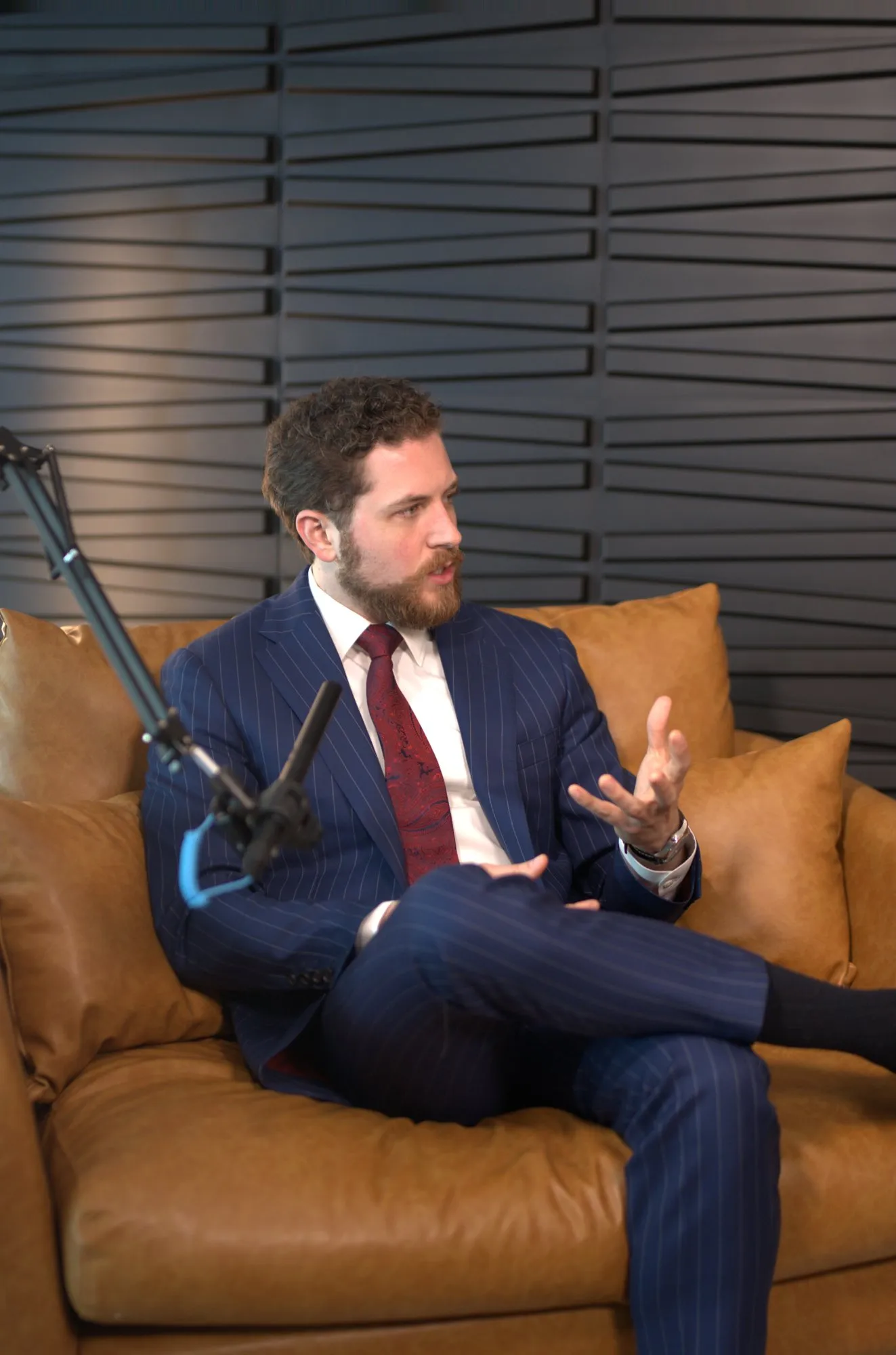 John Matthew Gillen in a navy pinstripe suit, speaking on the set of The Milk Road Show